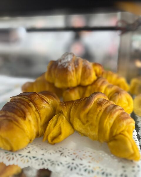 Croissants dourados sobre um naperon de papel rendado, no expositor do balcão.